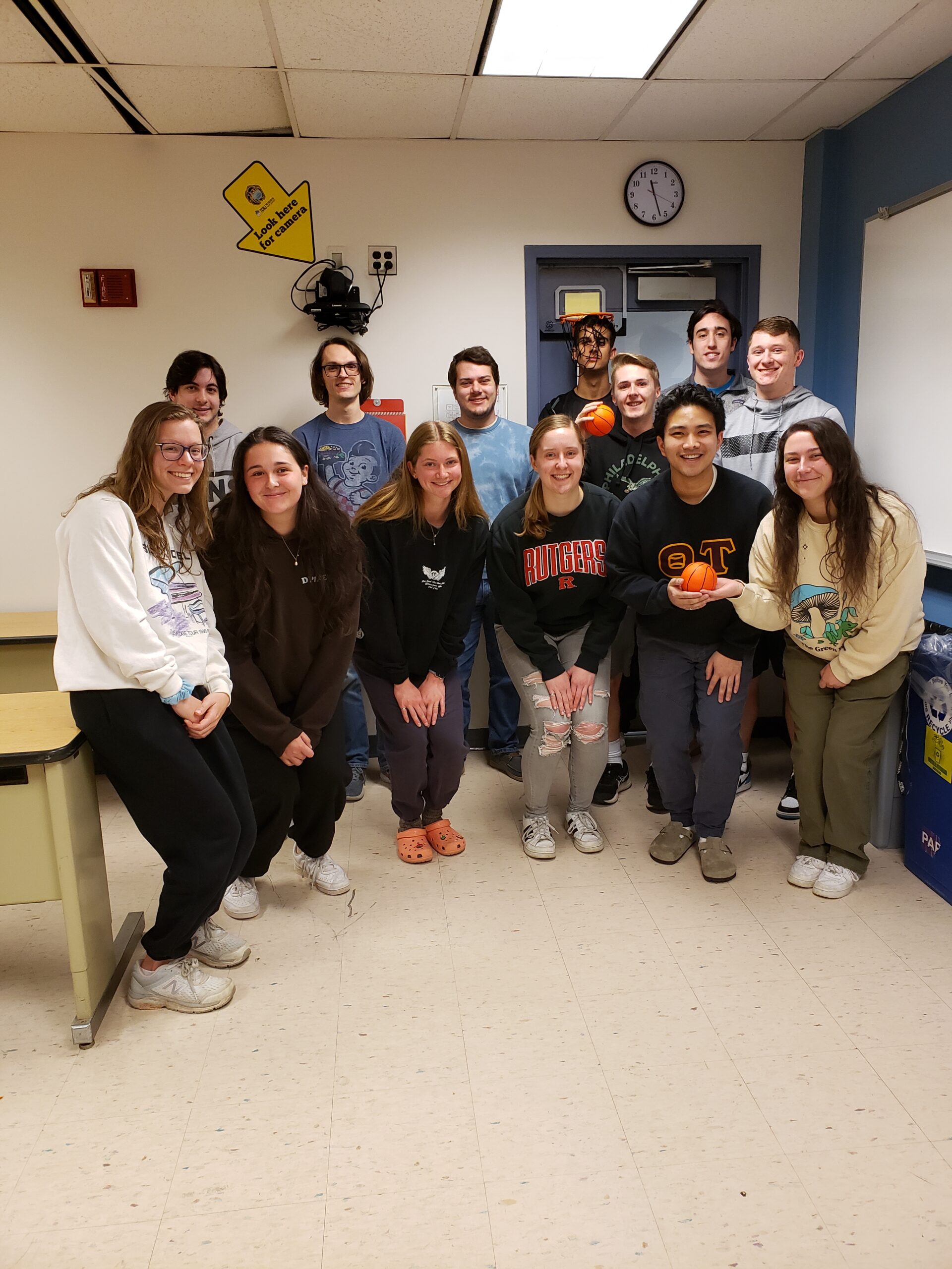 TCNJ XE members standing under a small basketball hoop and holding small orange balls.