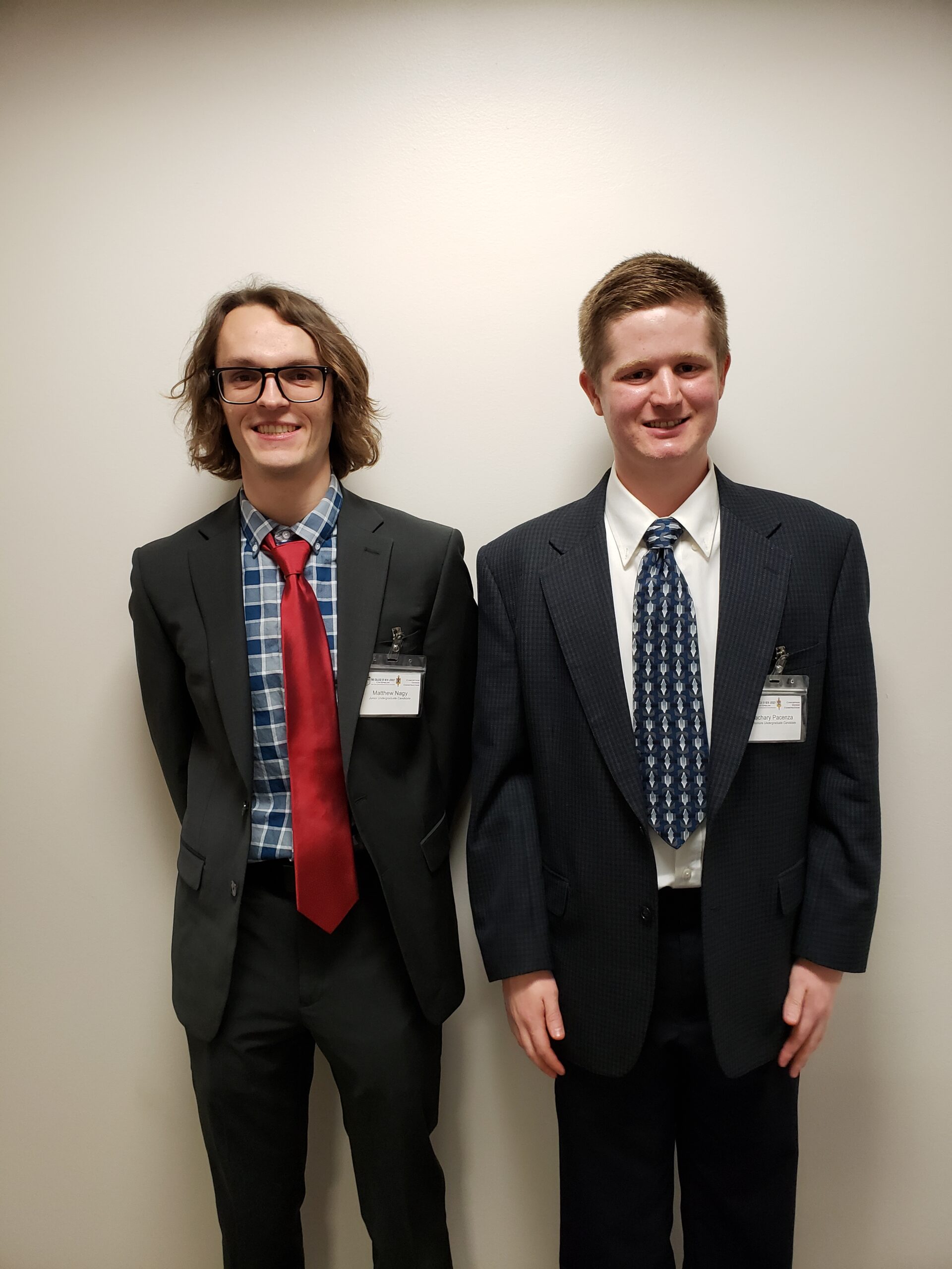 Matt Nagy (left) and Zach Pacenza (right) in business attire stand in front of a white wall.