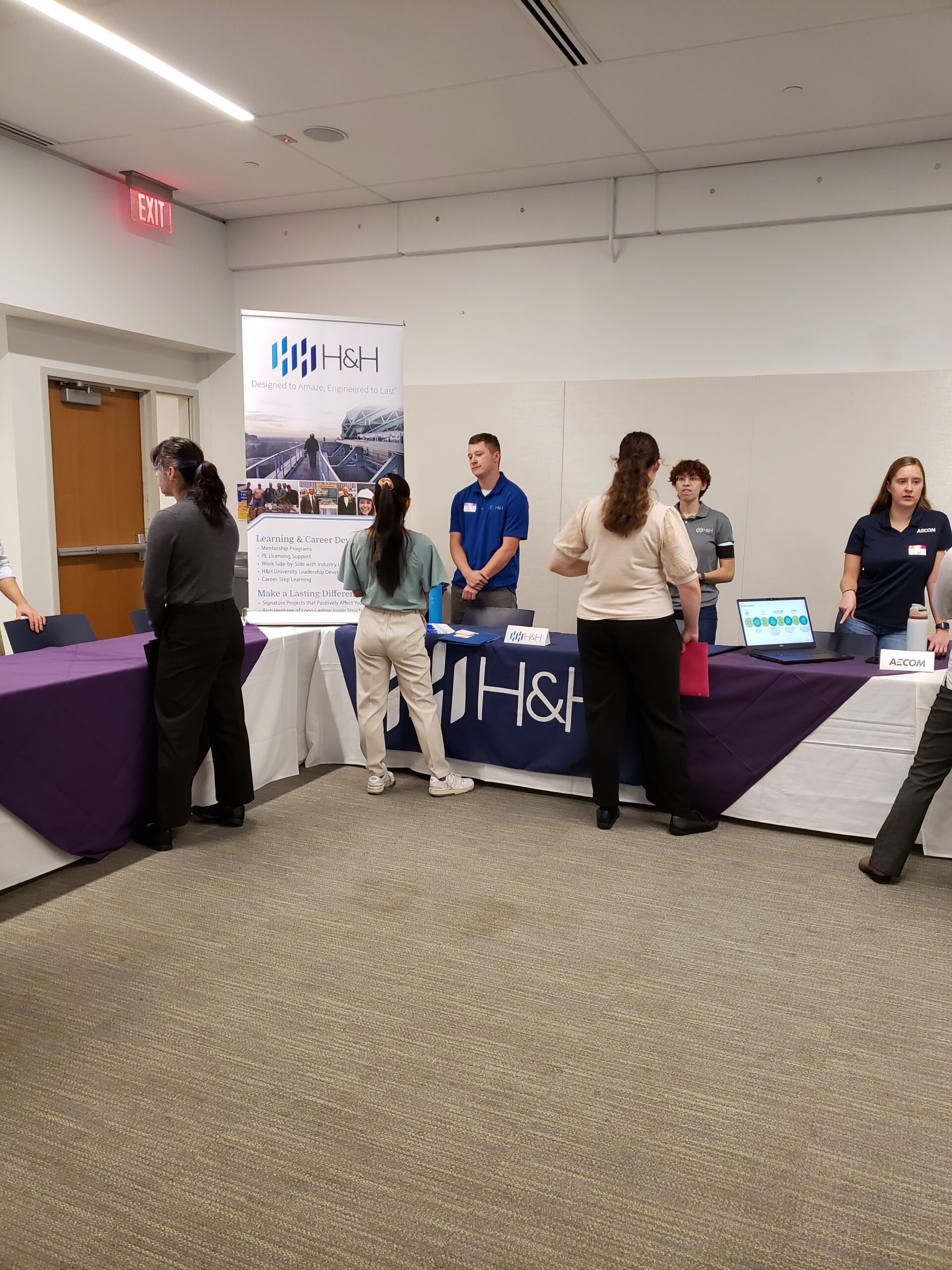 Students stand on one side of a table and alumni on the other during the networking event.