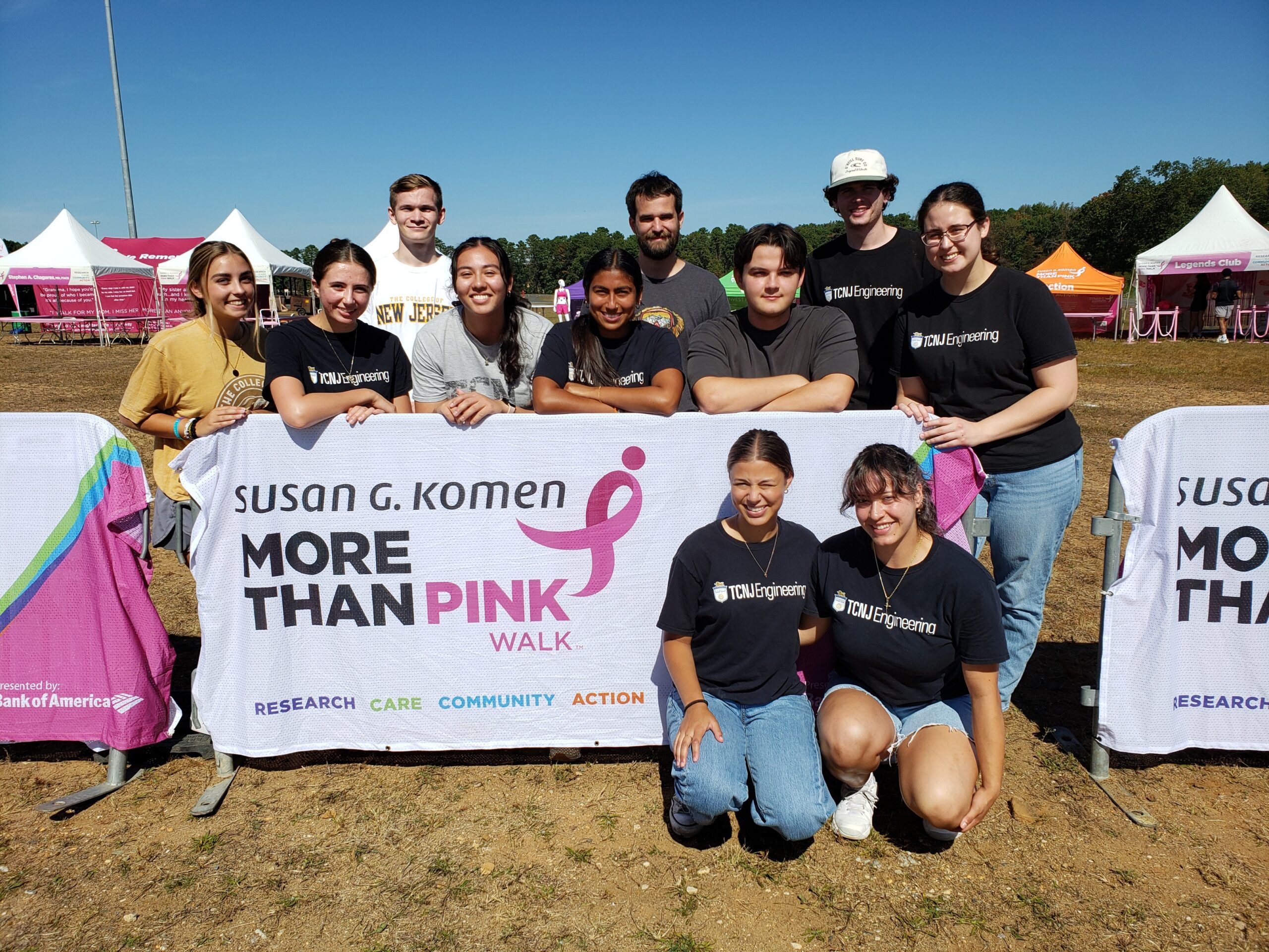 A group of 11 students stands around a banner that displays More Than Pink Walk logo.