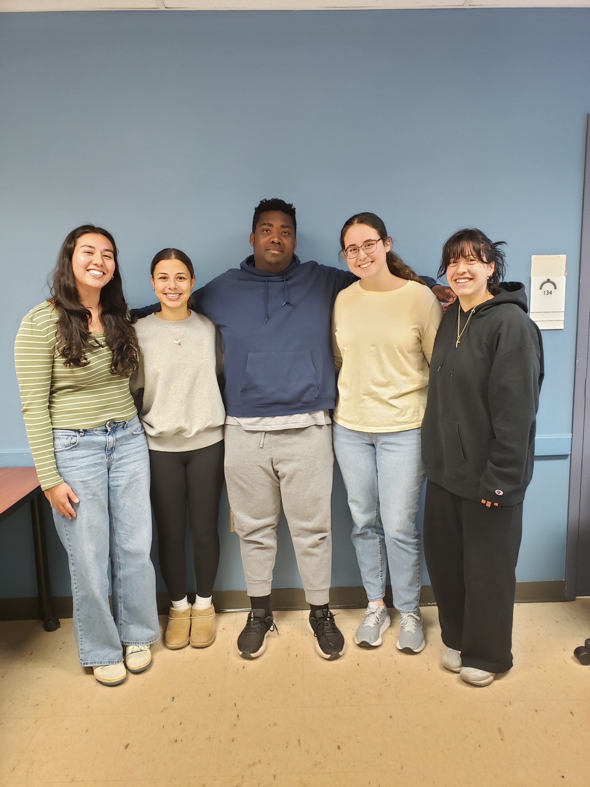 A group of five students stand in front of a blue wall.