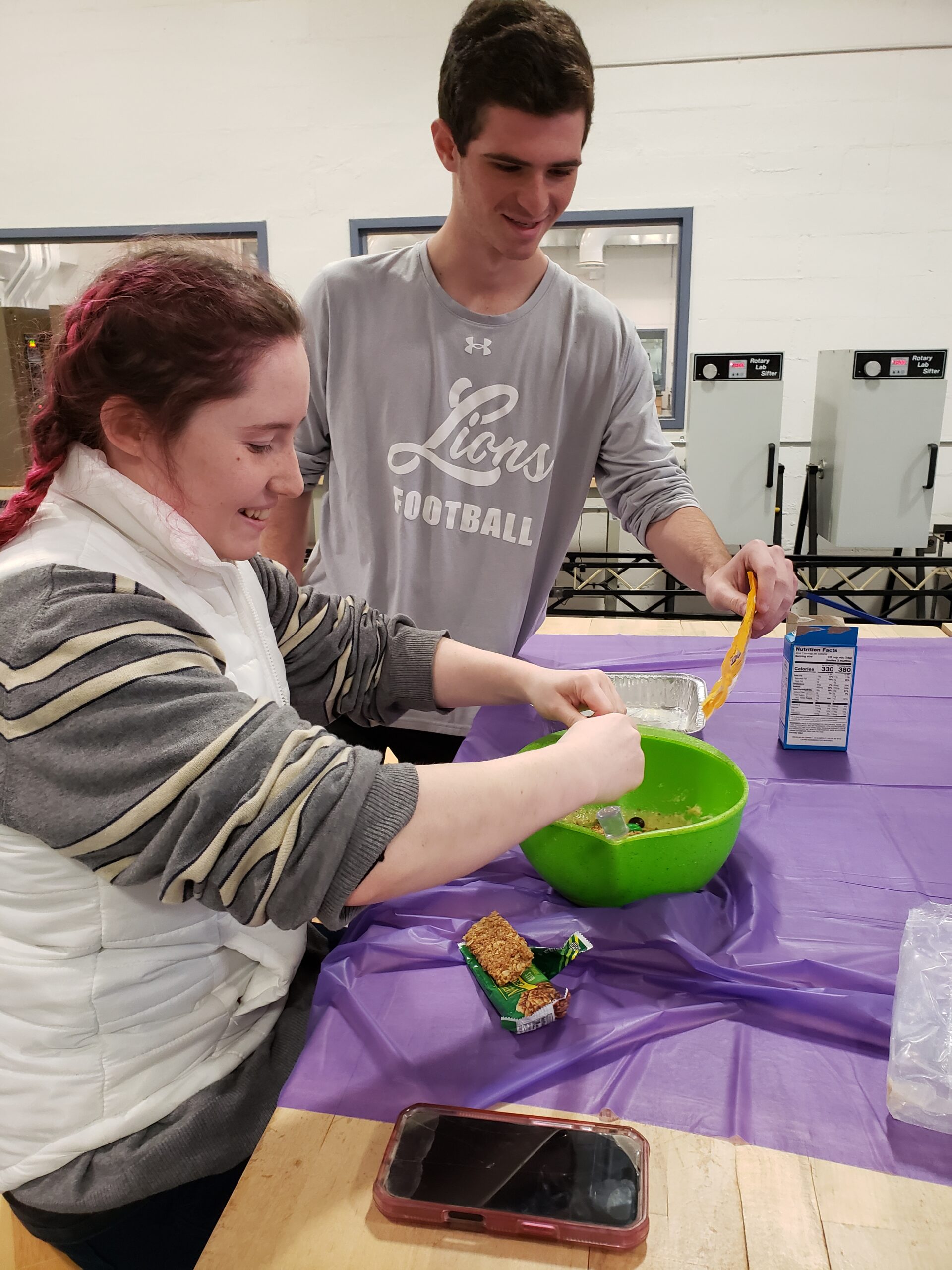 A male and a female student mix their cornbread in a bowl.