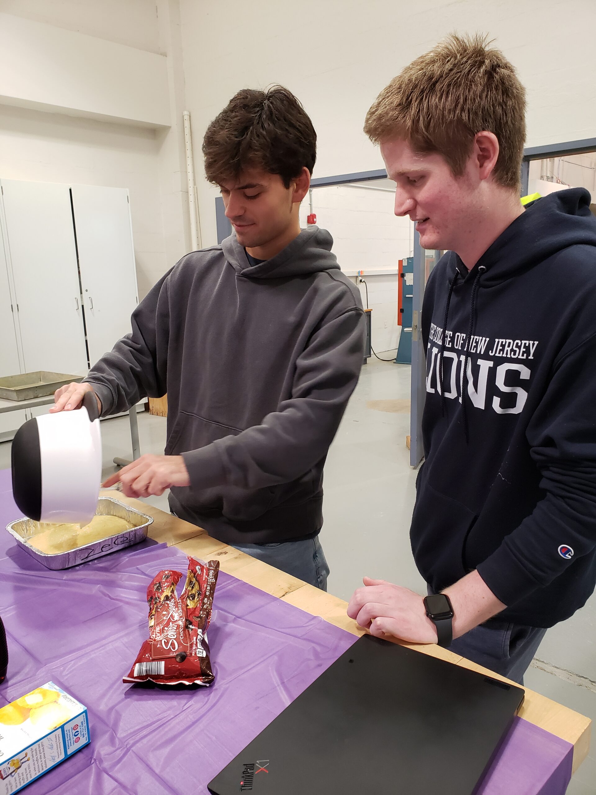 Two male students are filling their pan with cornbread mixture.