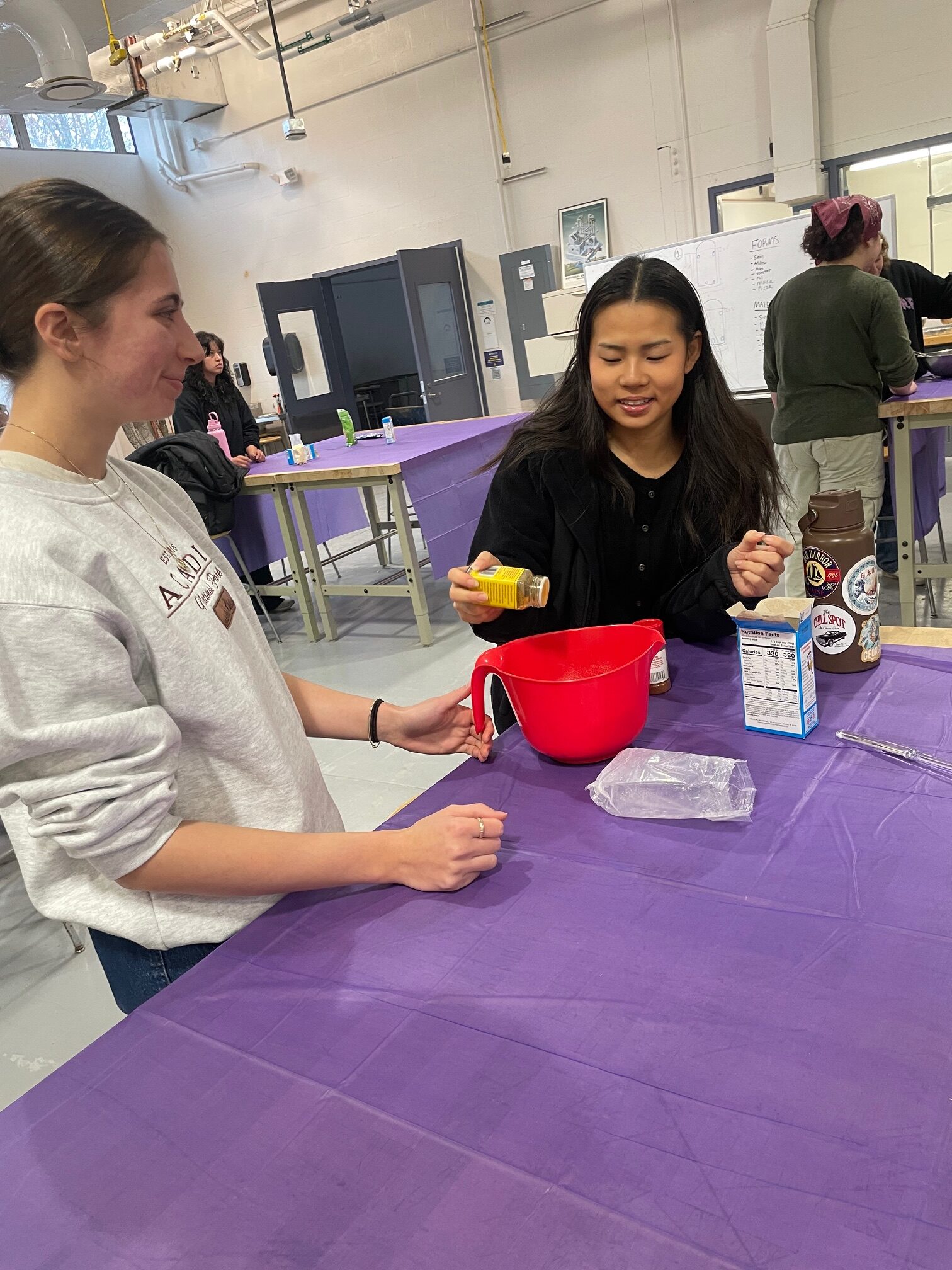 Two female students add ingredients to a cornbread mix