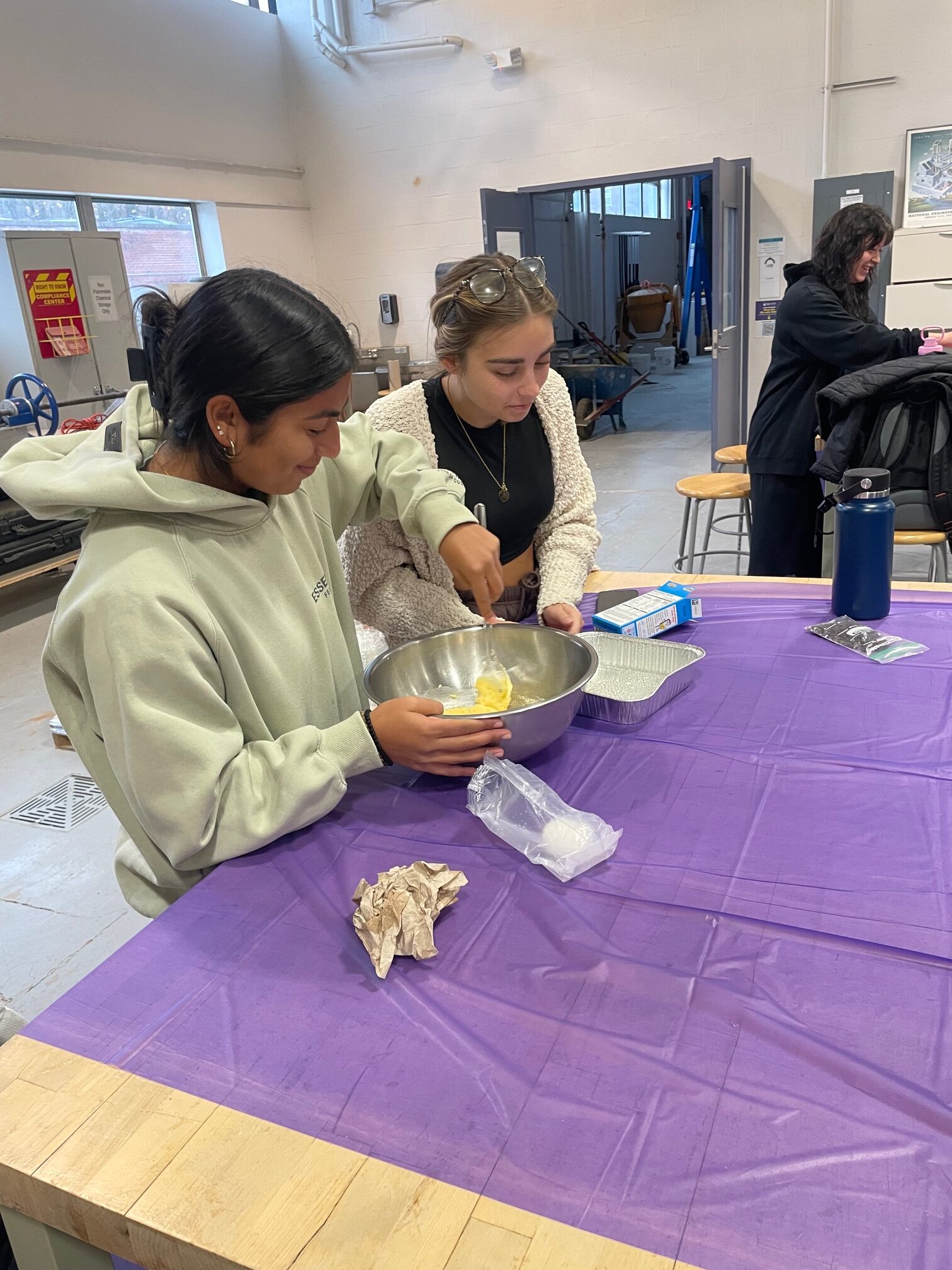 Two female students mix cornbread in a pan