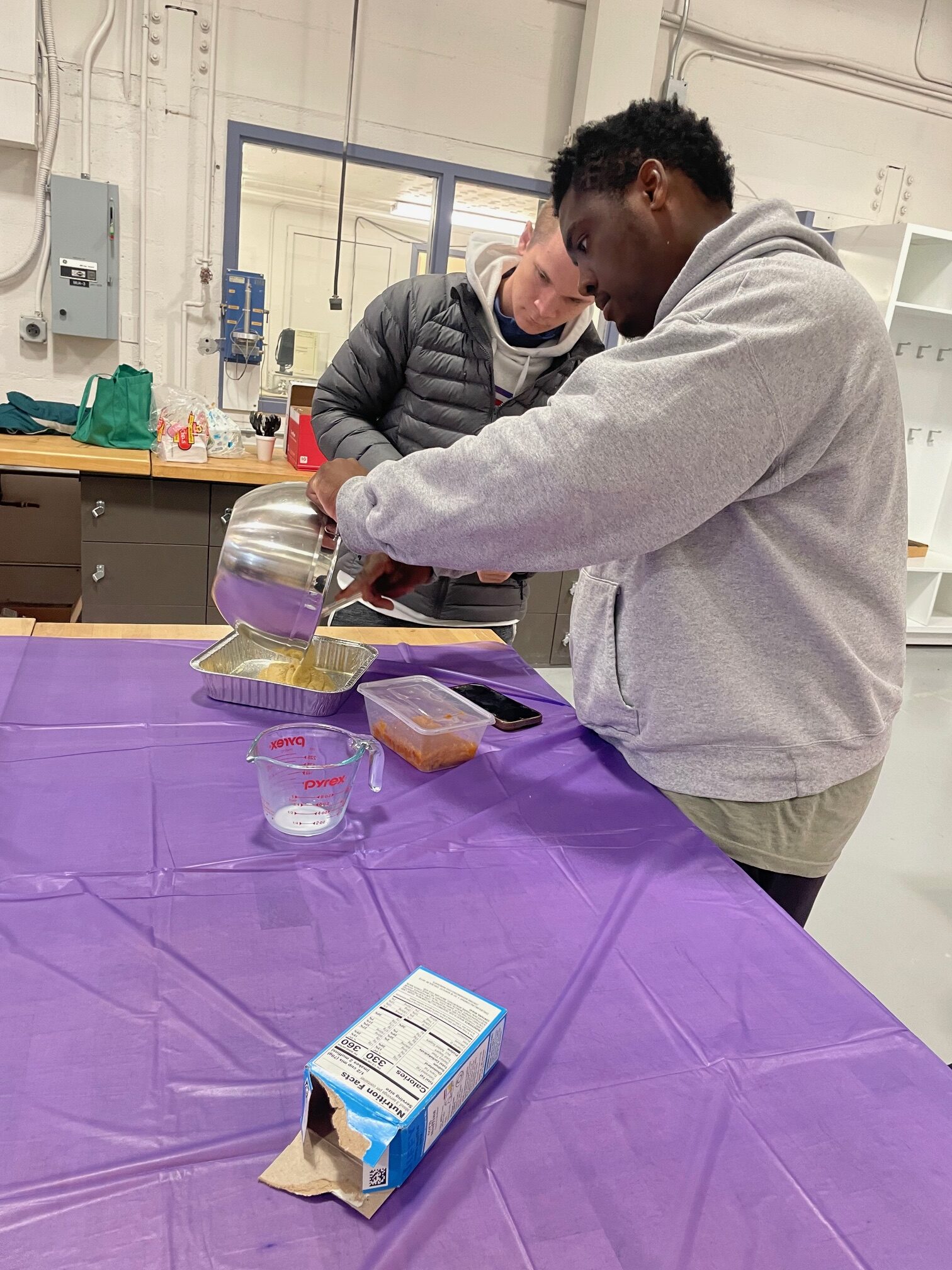 Two male students pour cornbread batter into a pan