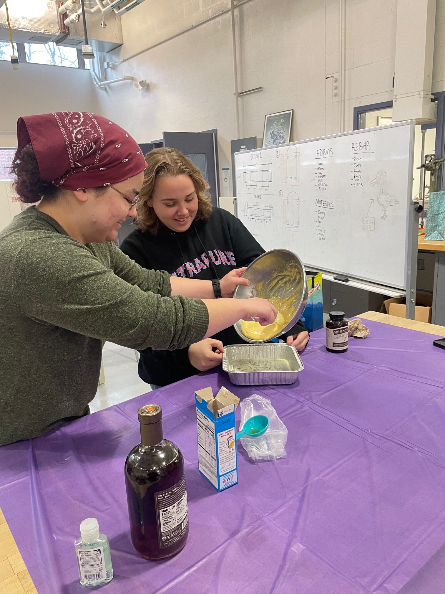 Two students pour cornbread batter into a pan