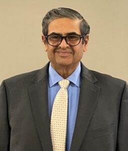A headshot of a man with glasses, blue short and yellow tie