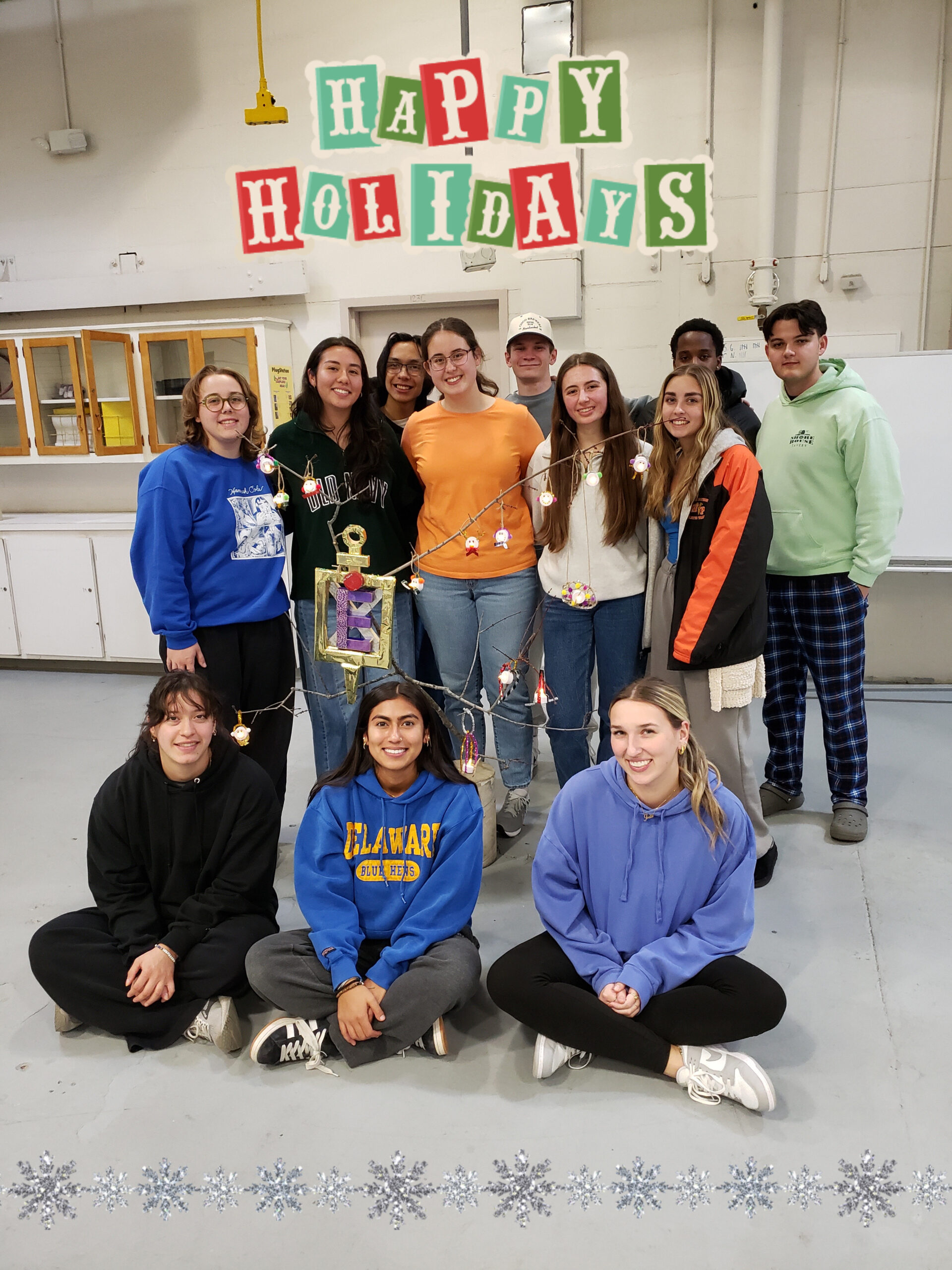 A group of students standing behind and sitting in front of a branch with ornaments