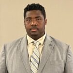 A headshot of an african american male student in a light gray suit and pale yellow shirt with yellow and gray striped tie