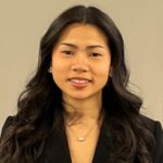 A headshot of a female student with long black hair in a dark suit wearing a necklace