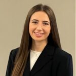 A headshot of a female student with long brown hair in a dark suit and white shirt
