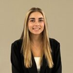 A headshot of a female student with long blond hair in a black suit and white shirt