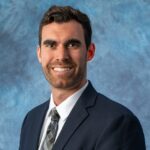 A headshot of a male in a dark suit and a white shirt