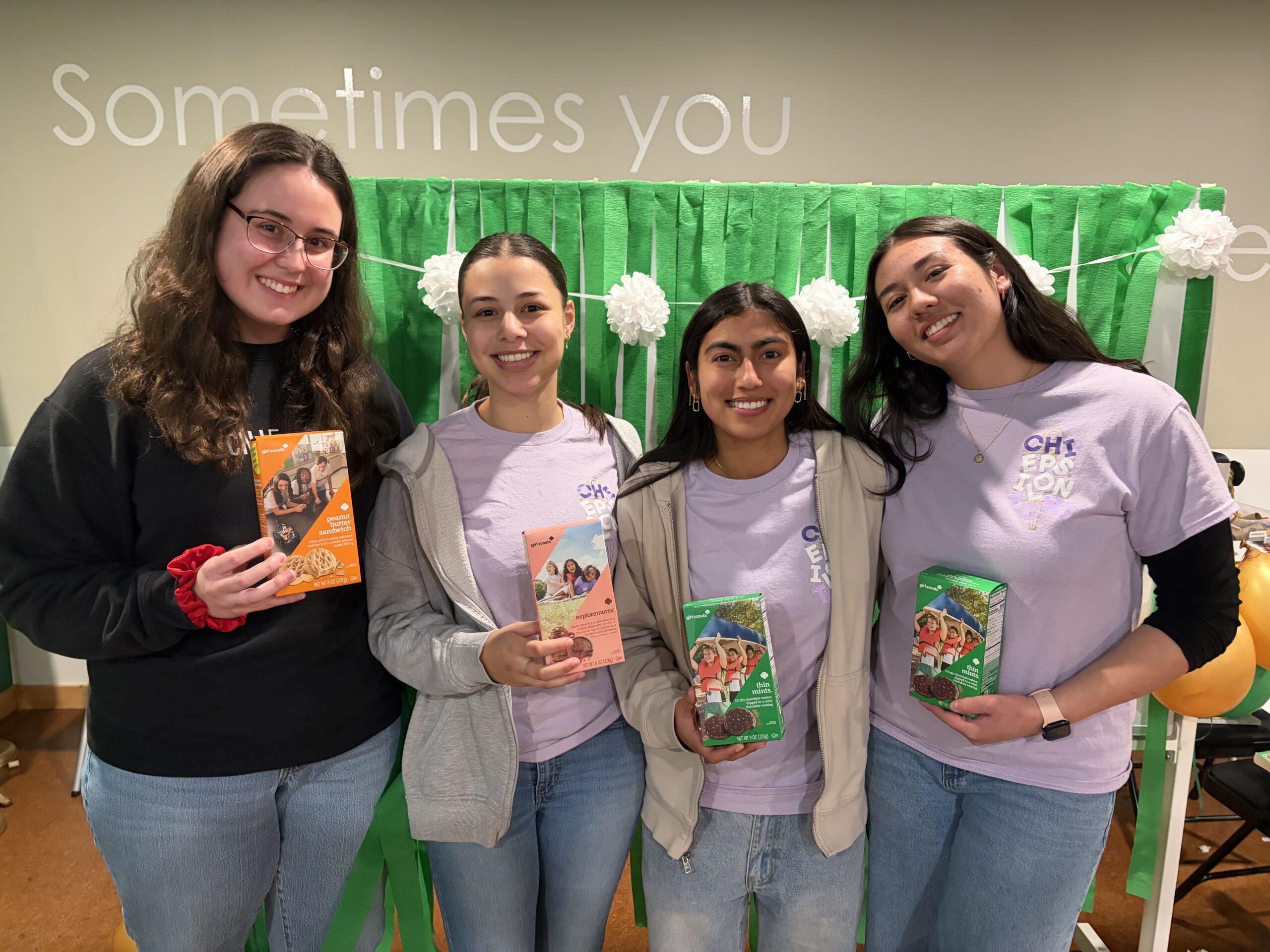 Four female students standing next to each other each holding a box of girl scouts cookies.