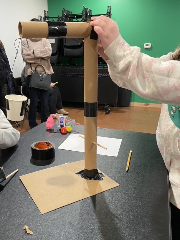 A structure built out of paper towel tubes shaped as an inverted L and taped to the table with black tape.