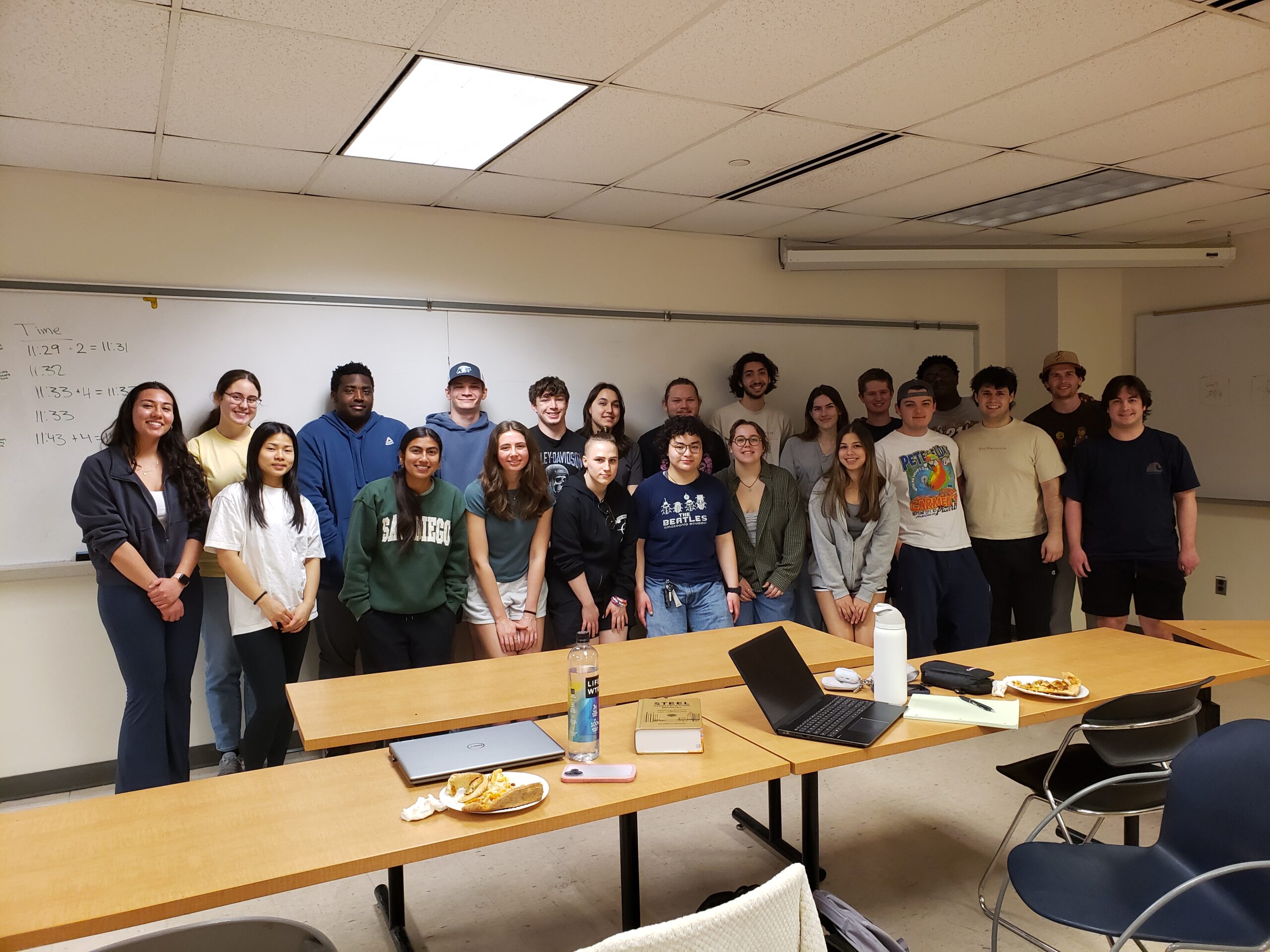 A large group of students standing in two rows in front of a long whiteboard.