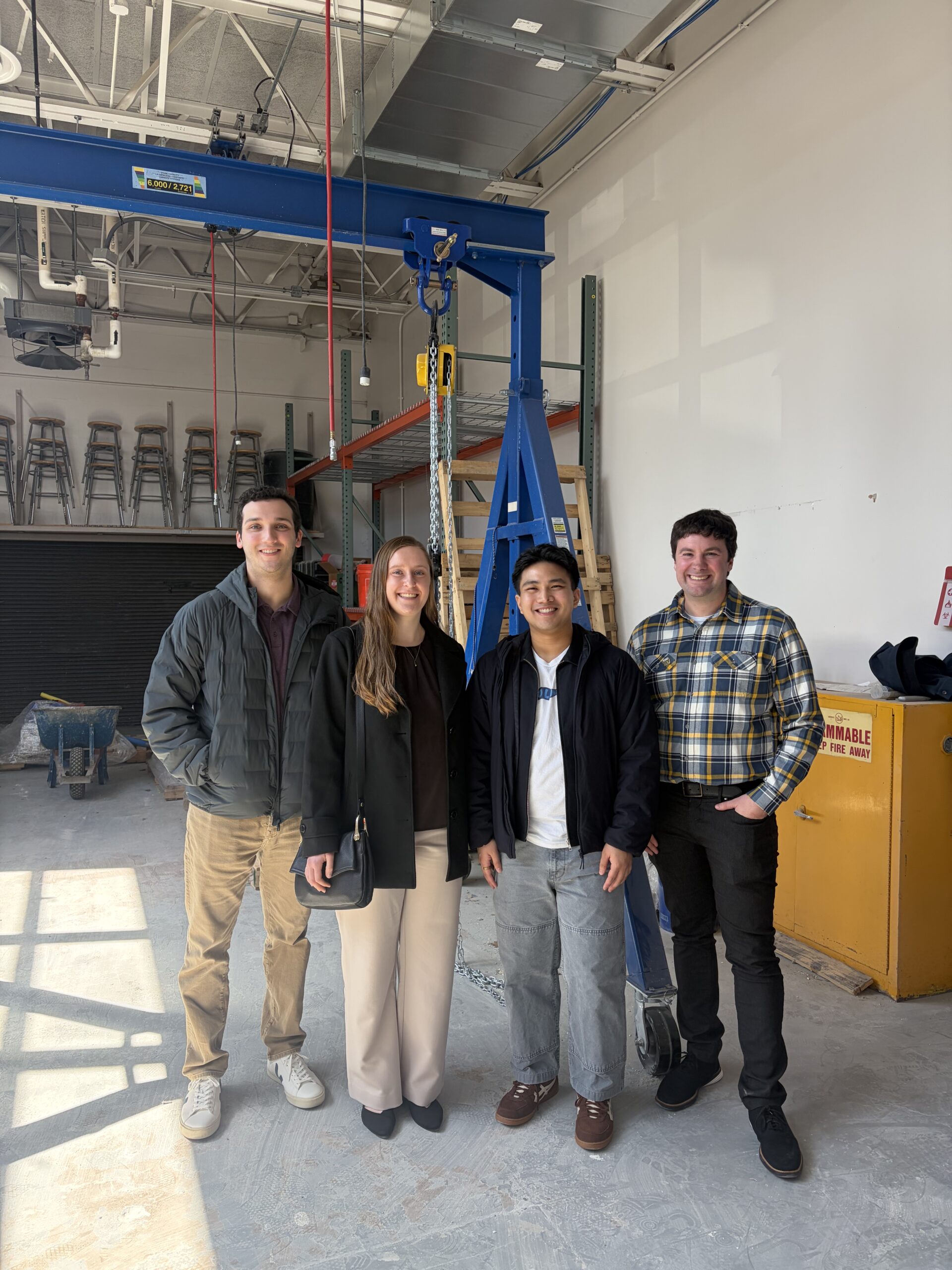 Three men and a woman stand in front of a load frame in a concrete laboratory at TCNJ. 
