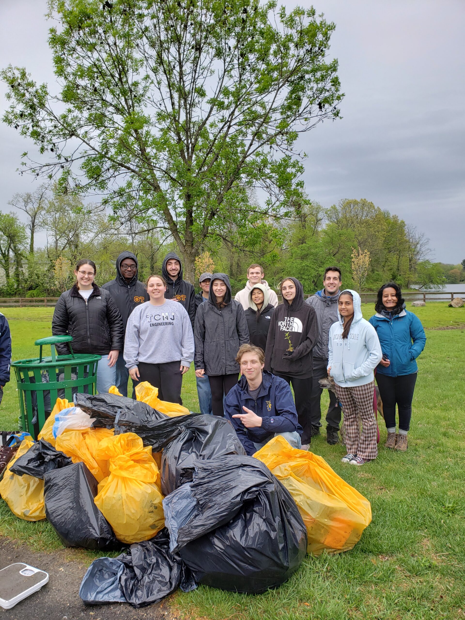 A group of students stands behind a large pile of garbage bags filled with litter that was collected around the lake.