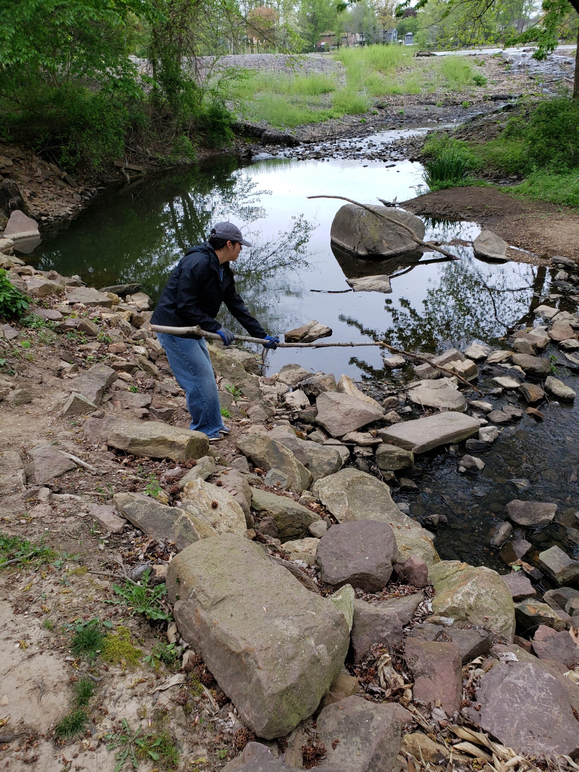 A female student tries to fish out a piece of trash with a long branch.