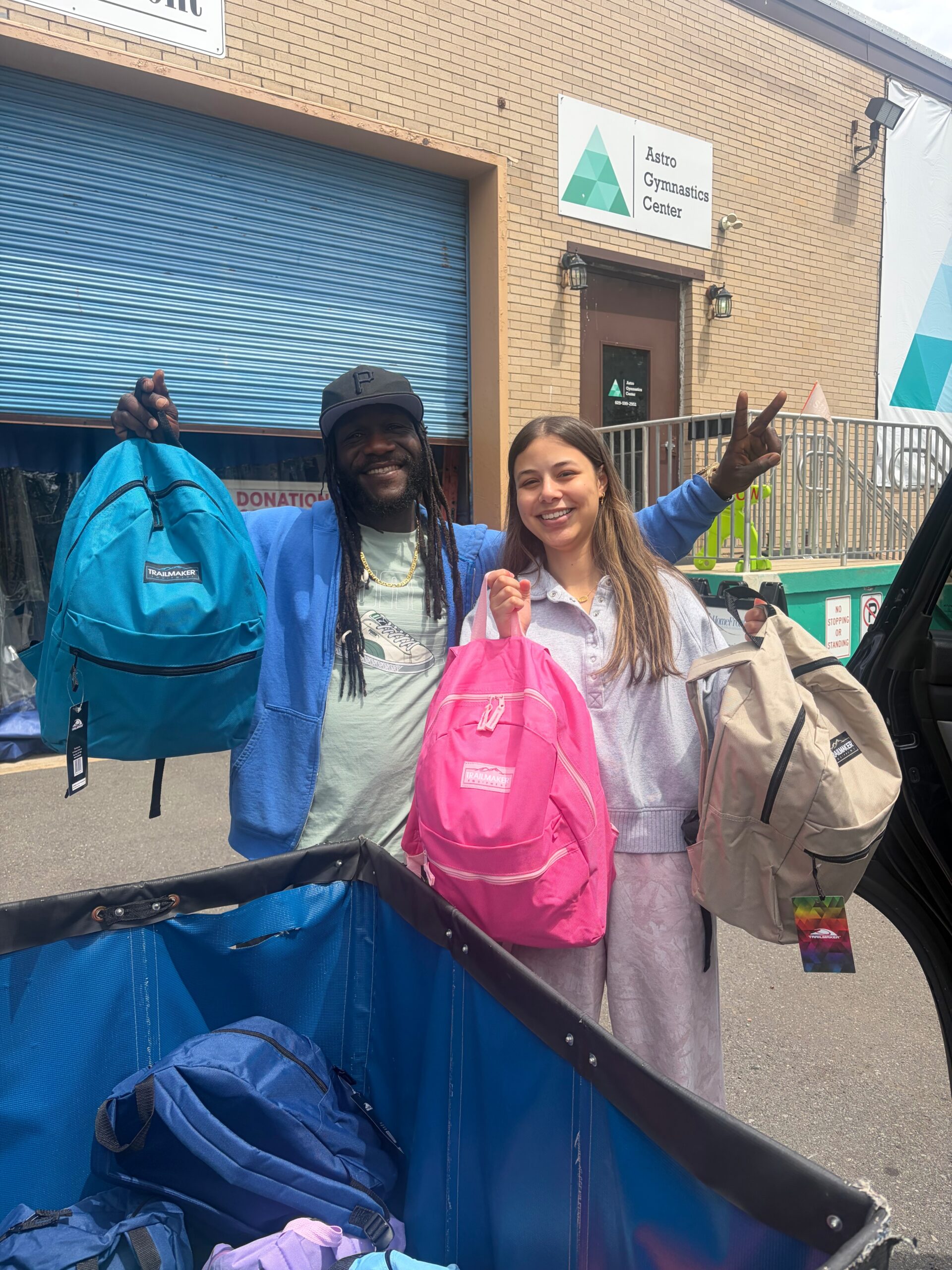 An african-american man and a female student stand next to each other holding backpacks
