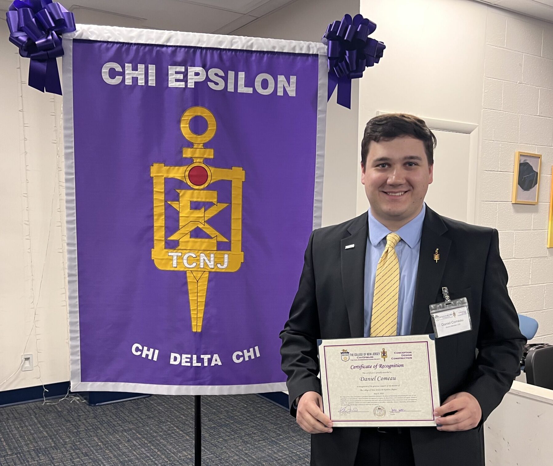 A man stands in front of an XE Banner holding a certificate