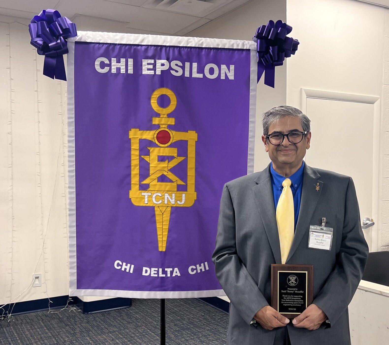 A man stands in front of the XE banner holding a plaque