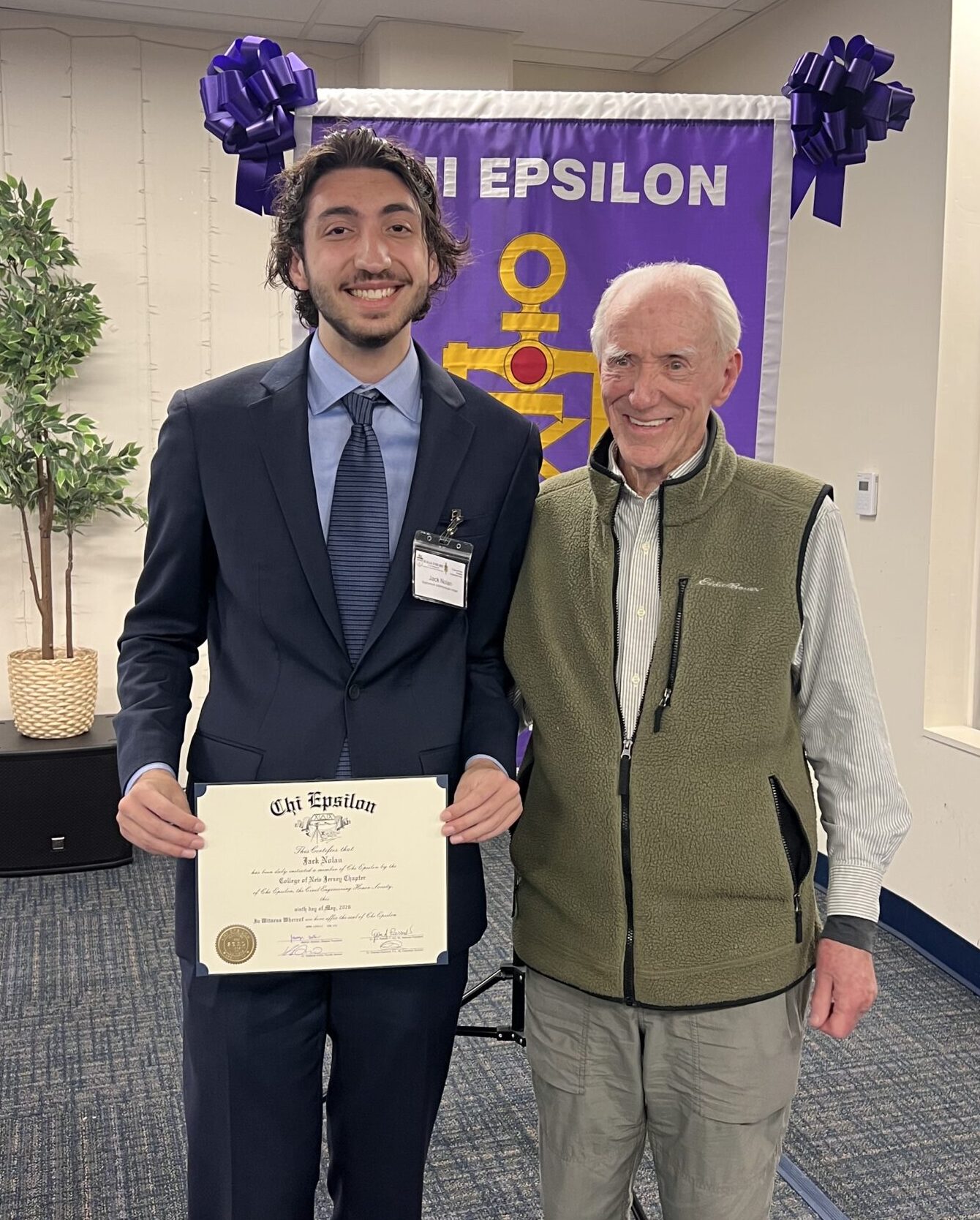 A sophomore student and his grandfather stand in front of the TCNJ XE banner.
