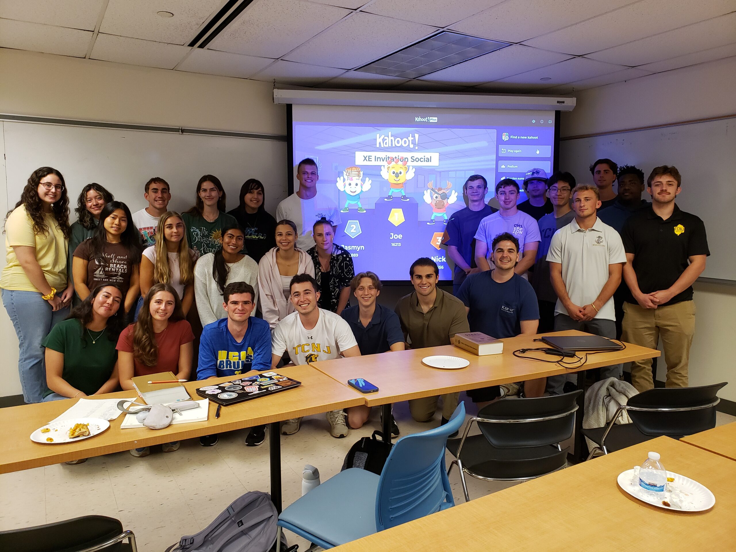 A group of students stand infront of a screen. Front row is squatting and the two rows behind them are standing.