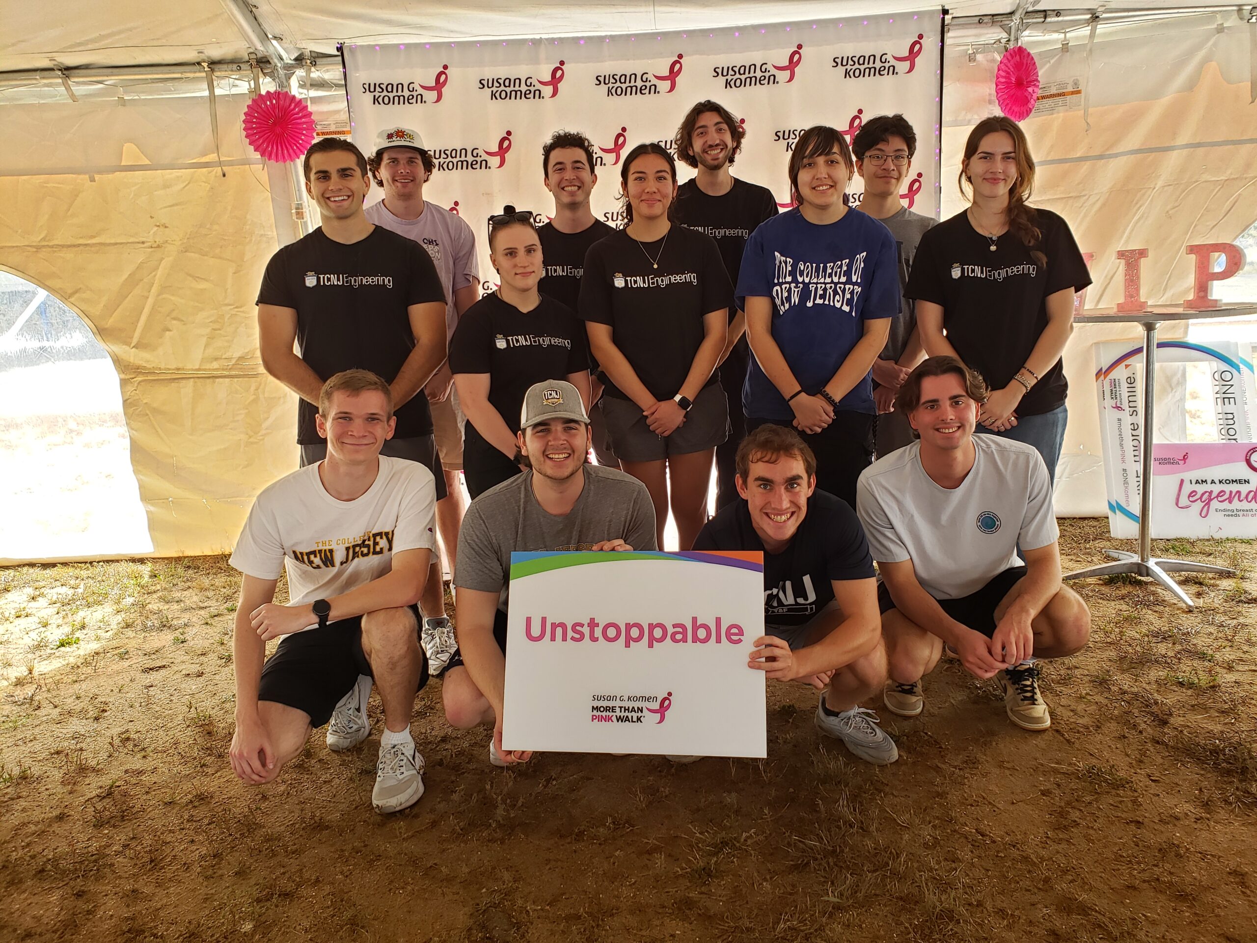 A group of students with four student crouching in the front and holding a sign that reads "Unstoppable". Other students stand behind them.