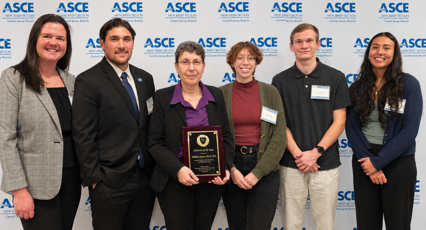 A group of 6 people standing in front of the white backdrop that has ASCE writtenn multiple times. THe third person from left holds the award.
